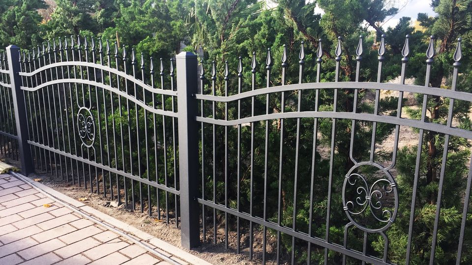 Schmuckzaun mit Spitzen und Ringornament vor einer Hecke